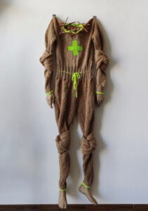 Contemporary art piece by Nanon Morsink titled "Full bodysuit (one size fits all)", made with rope, wool, knitting needles, hands, feet, and cord.